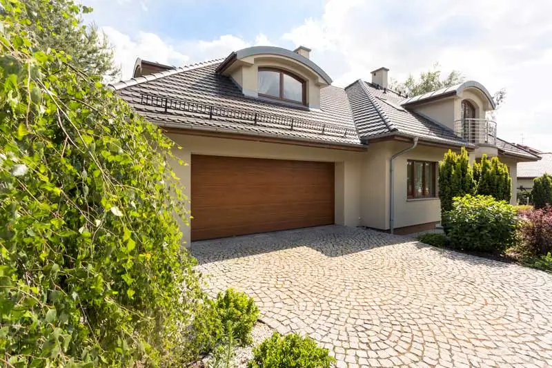 A high-end residential property featuring a custom wood-finish garage door and a cobblestone driveway. A garage door marketing agency helps businesses target homeowners looking for premium garage door installations