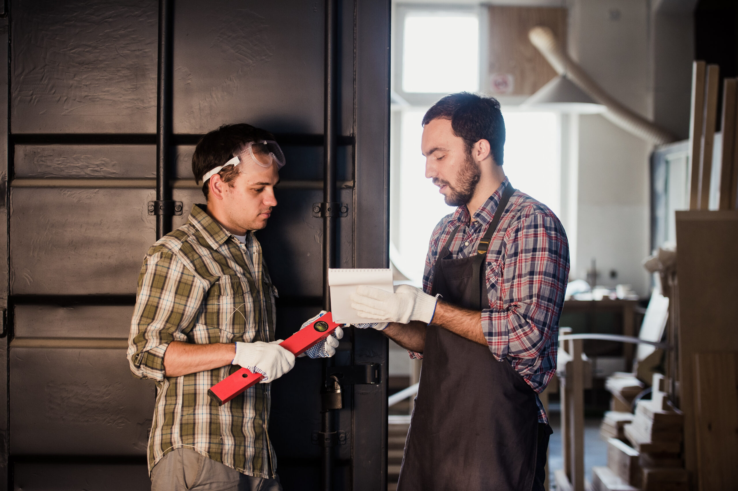 Two garage door contractors reviewing notes in a workshop — best way to advertise a garage door business through team collaboration and planning.